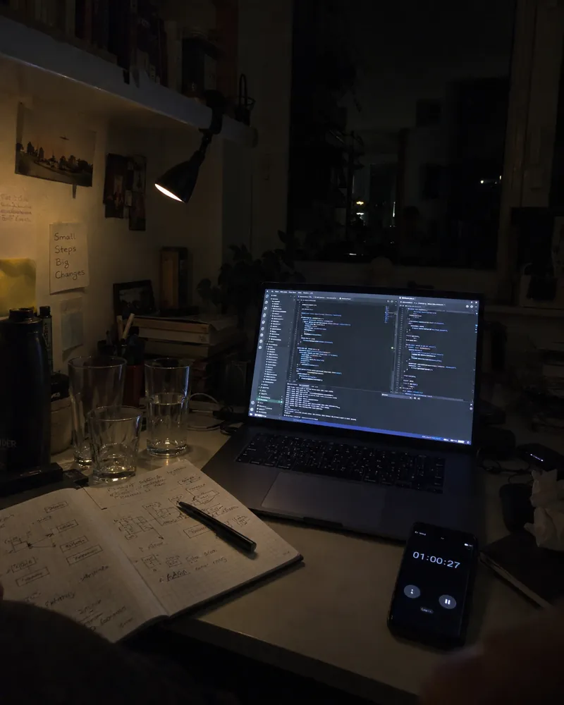 A study desk at 1am: a laptop full of code, a notebook and a running timer